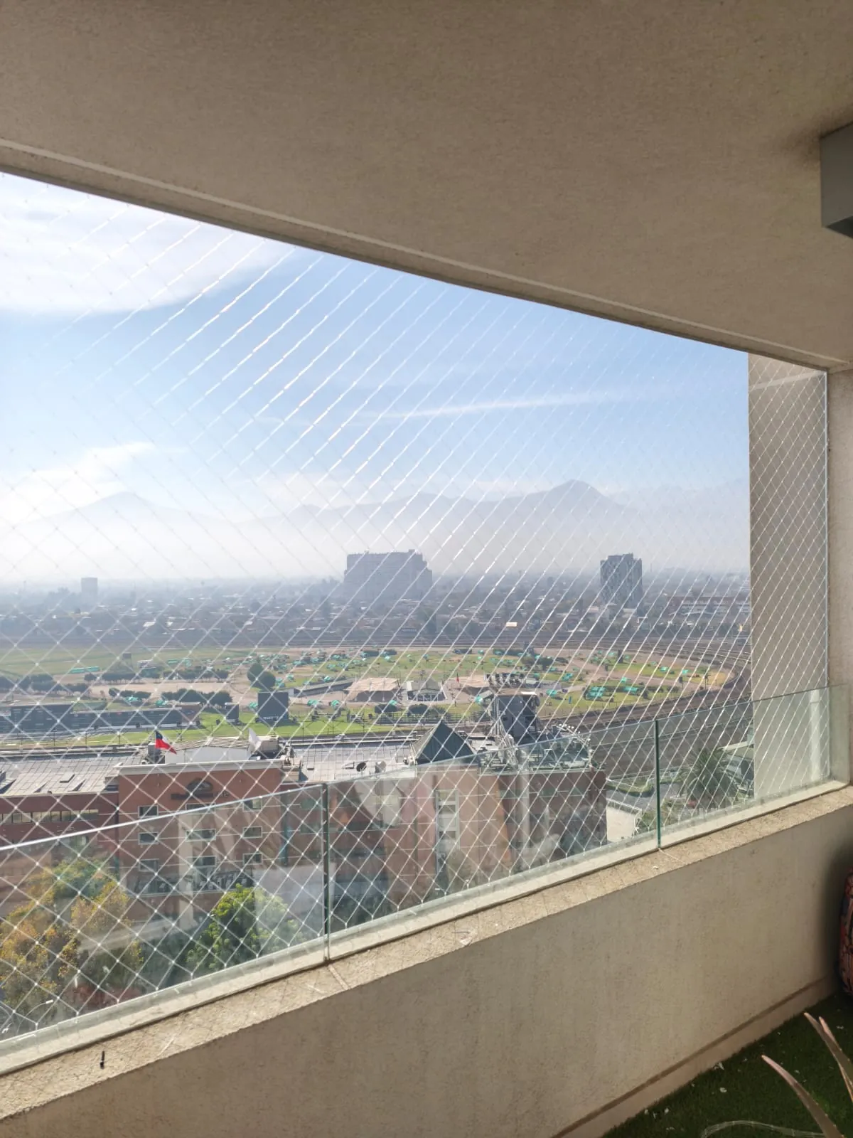 Malla de seguridad para balcones instalada en un departamento de Santiago, con baranda de vidrio y vista panorámica a la ciudad y la cordillera